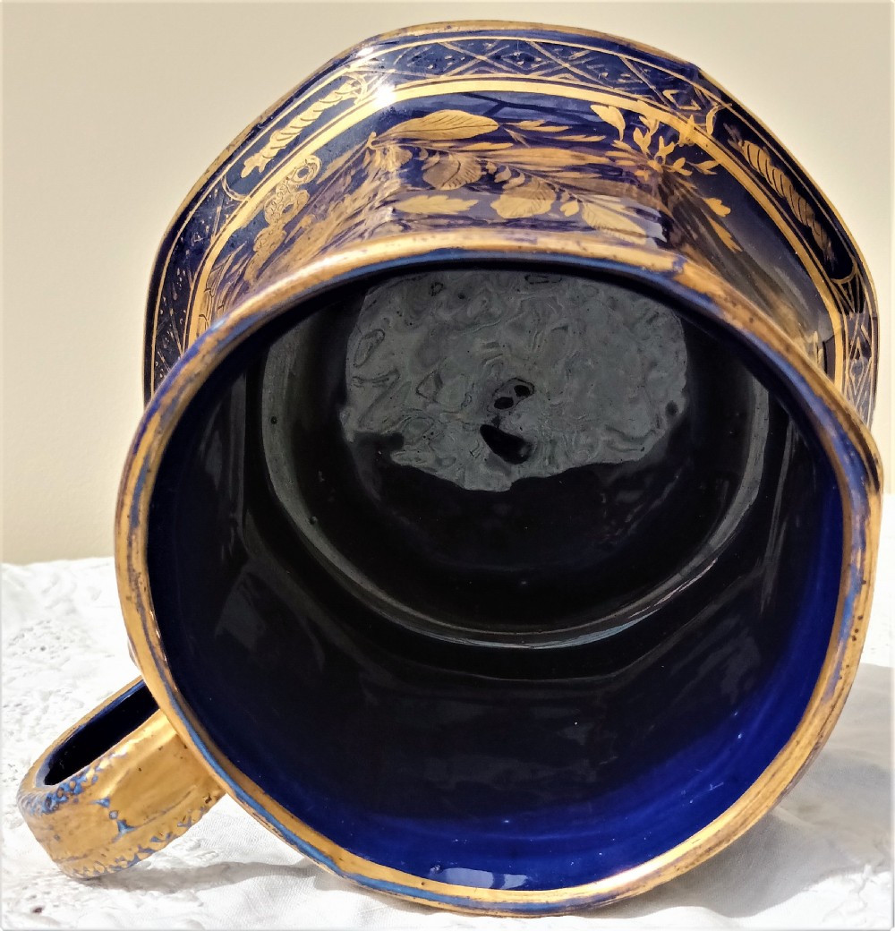 An antique cobalt blue ironstone mug featuring flared sides, a gilded scroll handle, and intricate gold floral motifs with a geometric border. View VI