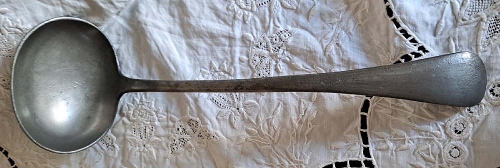An antique Victorian pewter basting ladle featuring a rounded deep bowl and an elongated flattened handle stem.