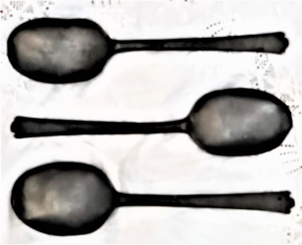 A dark carved oak wall-mounted spoon rack with flanking figural carvings, topped with a cross and floral motif, accompanied by three pewter trefid spoons. View IV