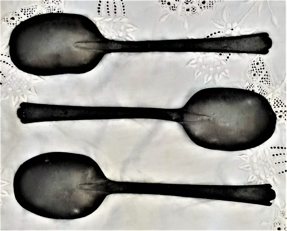 A dark carved oak wall-mounted spoon rack with flanking figural carvings, topped with a cross and floral motif, accompanied by three pewter trefid spoons. View V