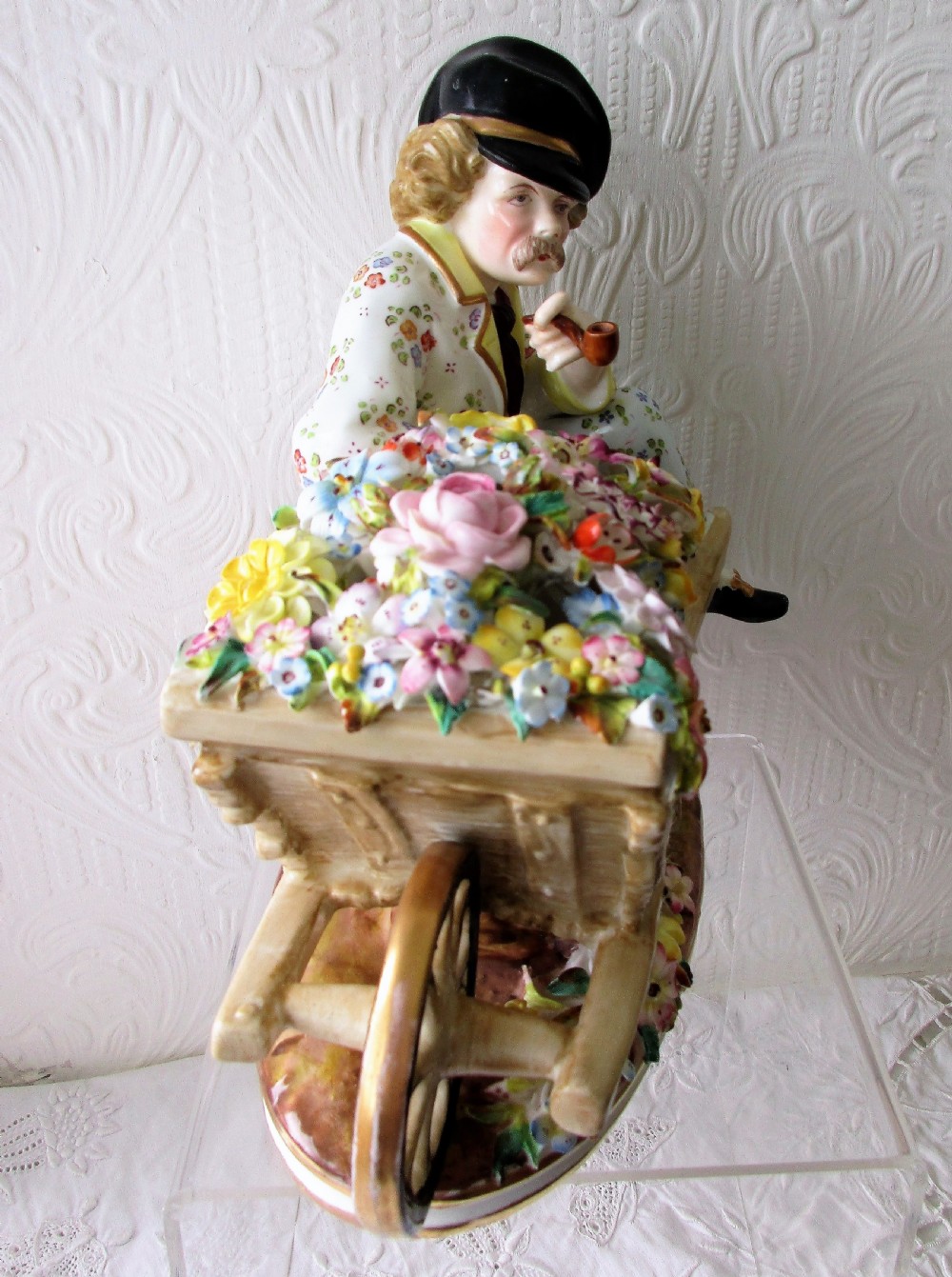 An English Victorian porcelain figurine depicting a seated male figure beside a wheelbarrow overflowing with colourful hand-crafted porcelain flowers. View IV
