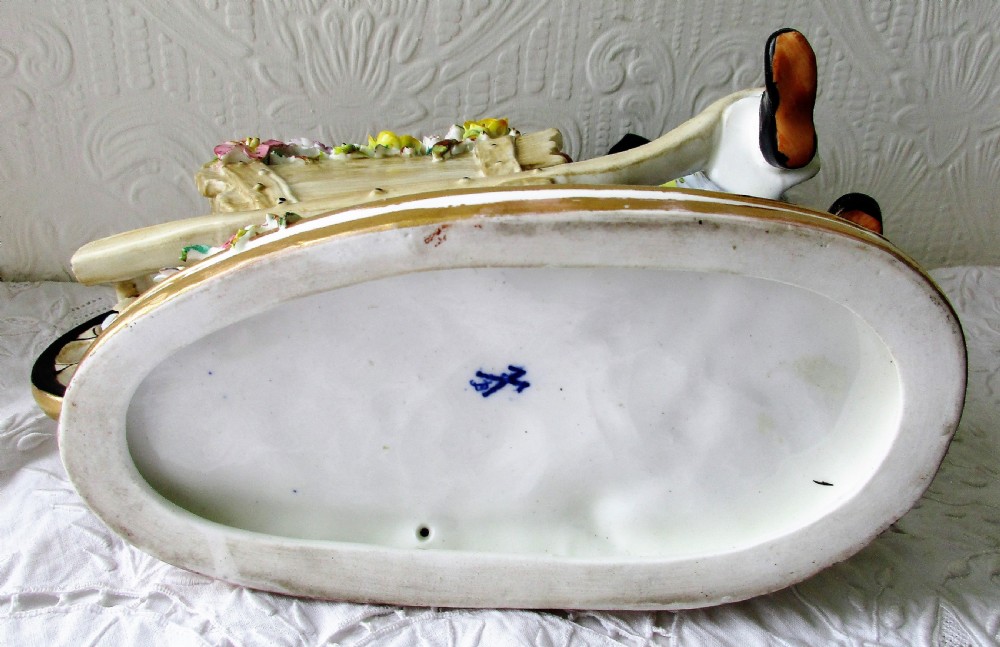 An English Victorian porcelain figurine depicting a seated male figure beside a wheelbarrow overflowing with colourful hand-crafted porcelain flowers. View V