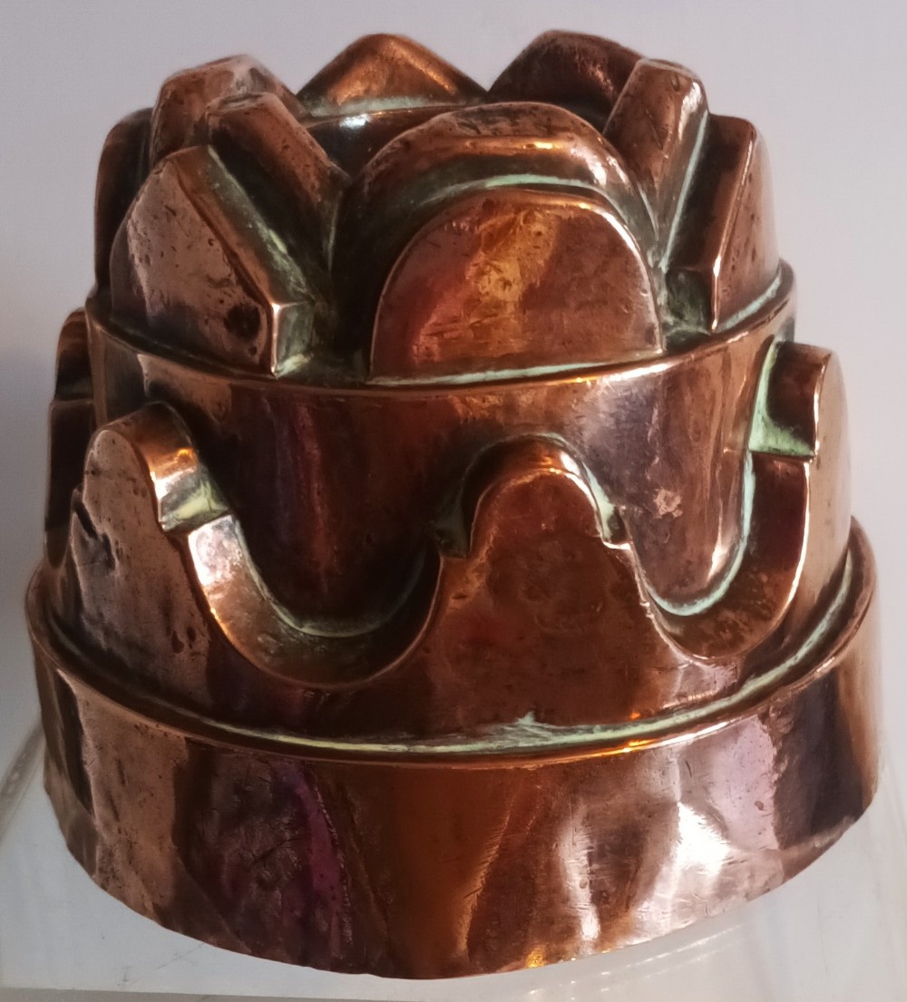 A tiered Victorian copper jelly mould featuring geometric fluted arches and a central crown pattern.
