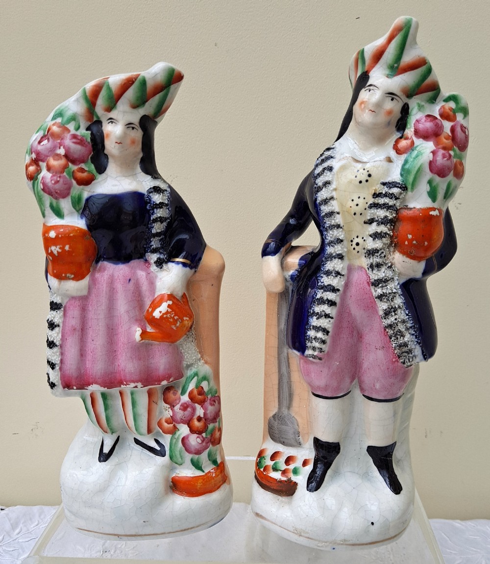 A pair of antique Victorian Staffordshire earthenware figures depicting a male and female gardener dressed in colourful attire holding flowers.