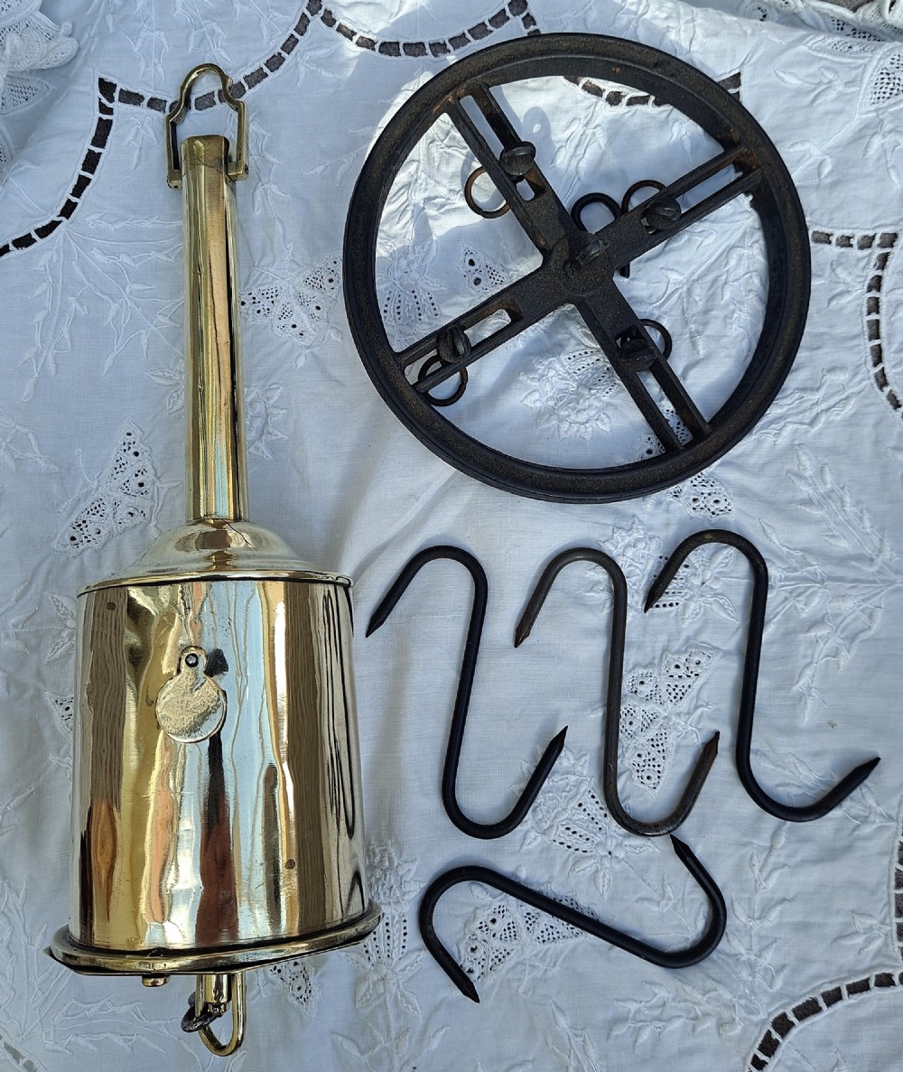A brass bottle-shaped clockwork spit jack displayed alongside an iron mounting wheel and four wrought iron hooks.