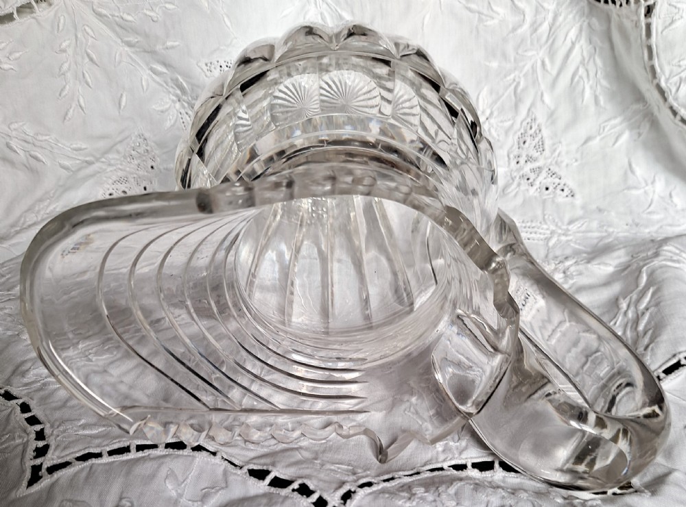 A clear antique cut glass water jug featuring step-cut neck rings, deep vertical facet cutting, a scalloped rim, and a sturdy loop handle. View VI