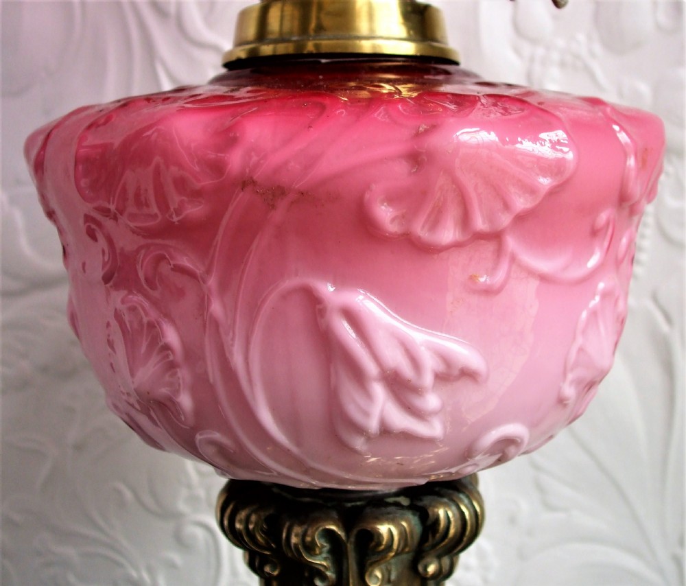 A Victorian oil lamp featuring a fluted brass column base, an embossed pink glass oil reservoir, and a ruffled cranberry glass shade. View III
