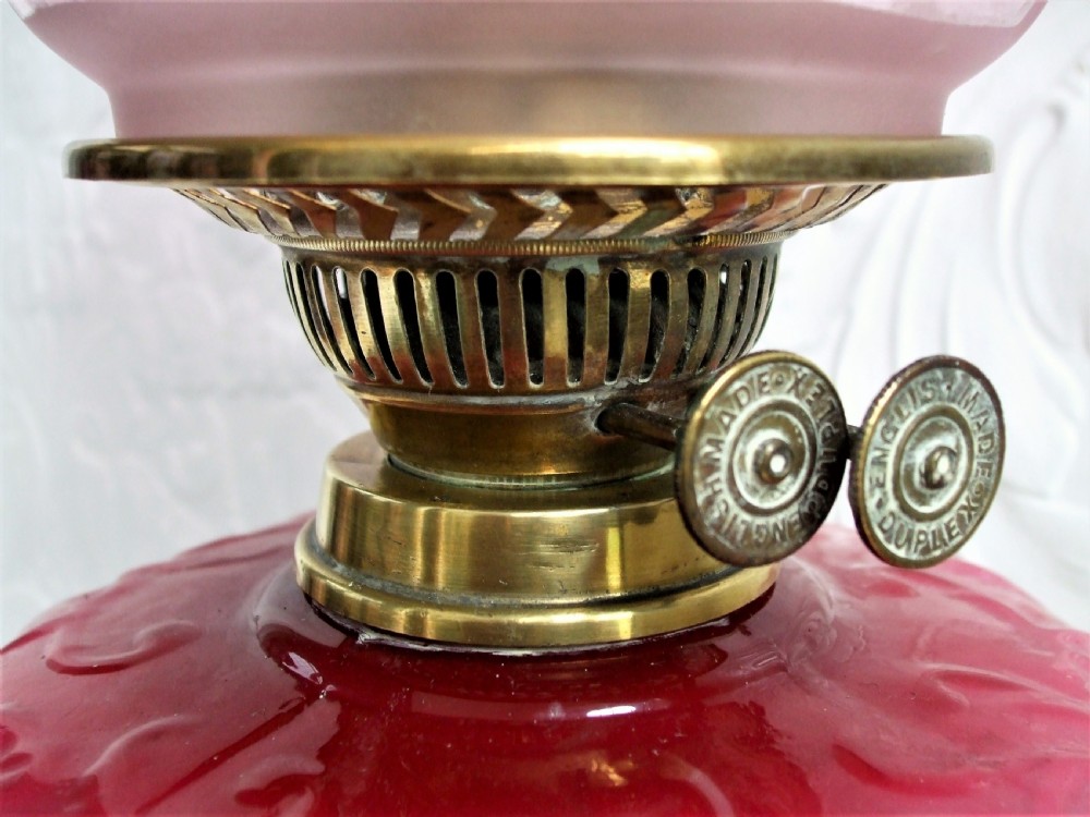 A Victorian oil lamp featuring a fluted brass column base, an embossed pink glass oil reservoir, and a ruffled cranberry glass shade. View IV