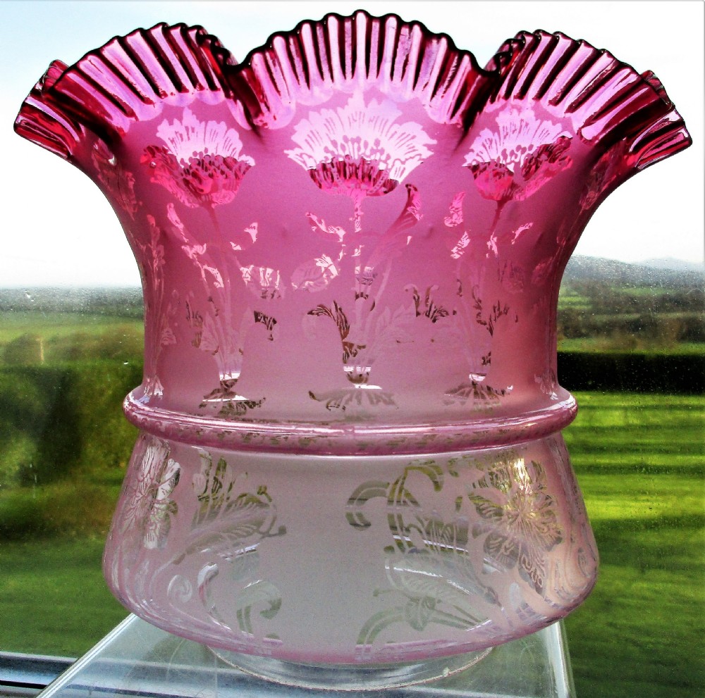 A Victorian oil lamp featuring a fluted brass column base, an embossed pink glass oil reservoir, and a ruffled cranberry glass shade. View V