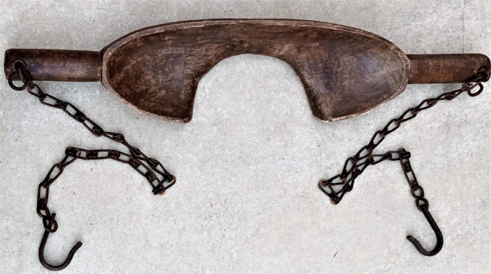 A carved dark beech wooden shoulder yoke featuring a central neck cutout and two attached iron chains with hooks.