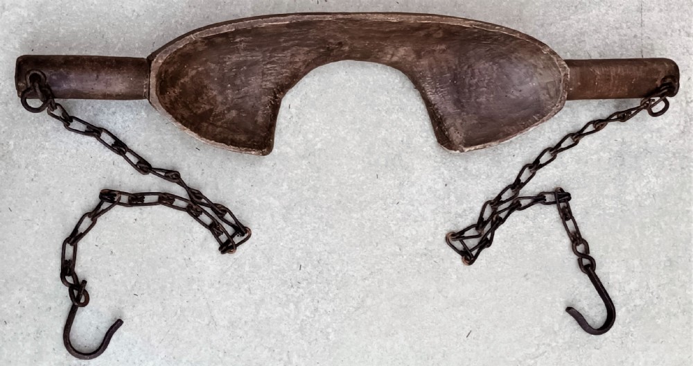 A carved dark beech wooden shoulder yoke featuring a central neck cutout and two attached iron chains with hooks. View V
