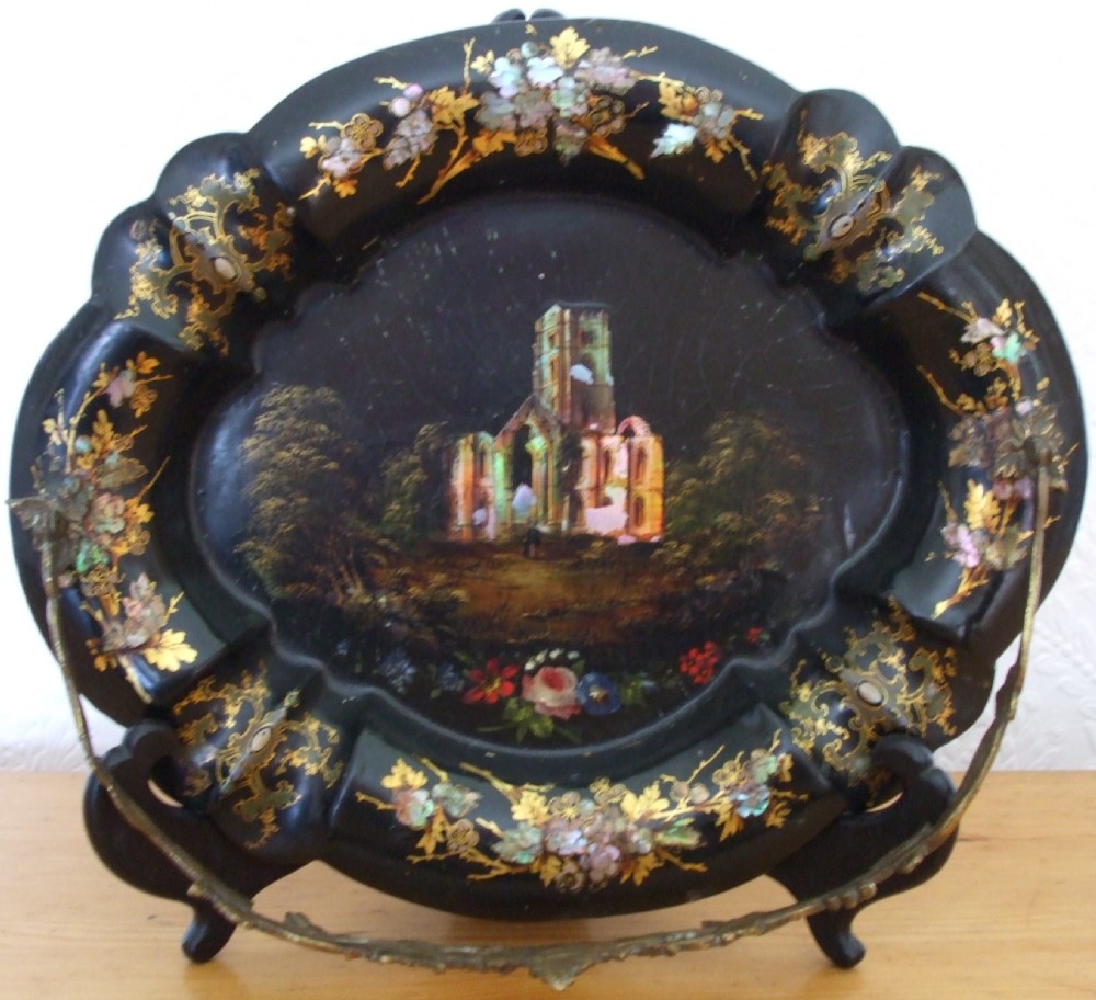 An oval black papier-mache card basket featuring scalloped edges, mother-of-pearl floral inlays, gilding, a painted abbey ruin vignette, and a metal swing handle.