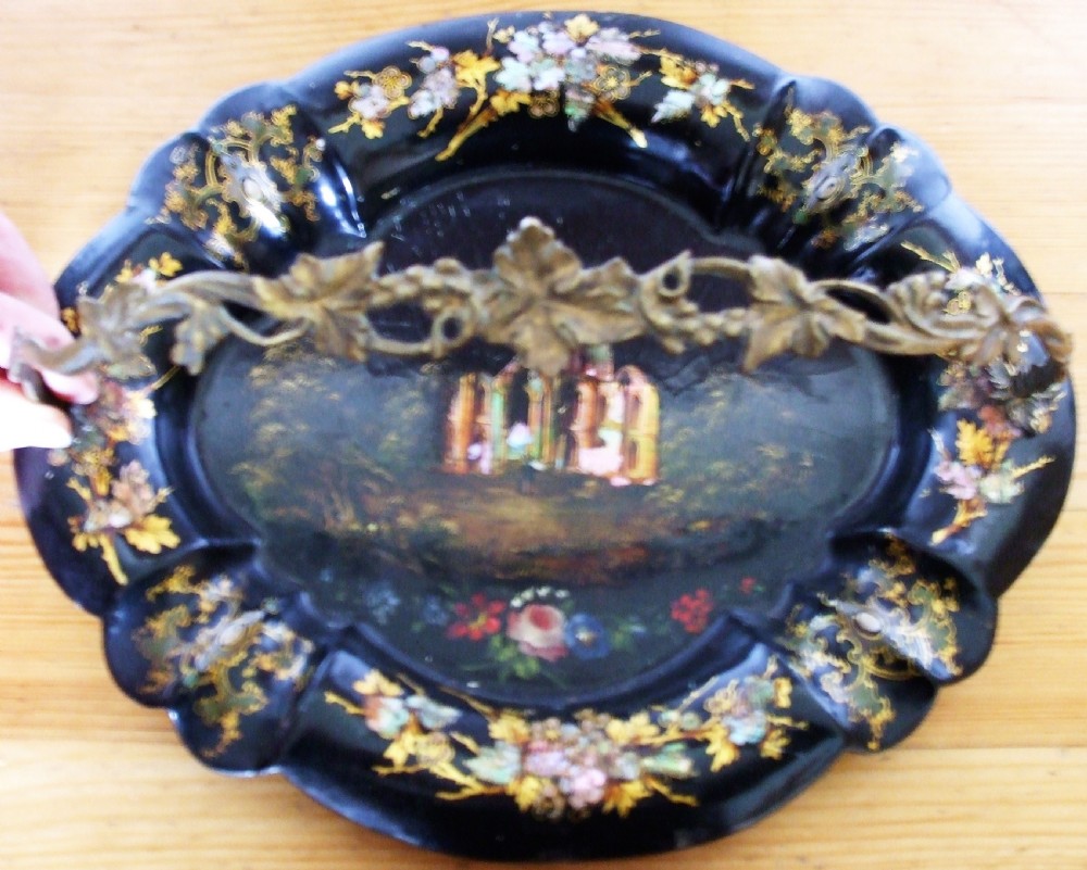 An oval black papier-mache card basket featuring scalloped edges, mother-of-pearl floral inlays, gilding, a painted abbey ruin vignette, and a metal swing handle. View II