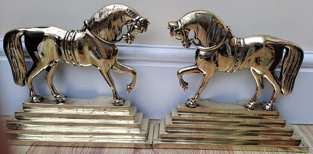 A pair of polished cast brass equestrian horses facing each other, mounted on stepped rectangular plinths.