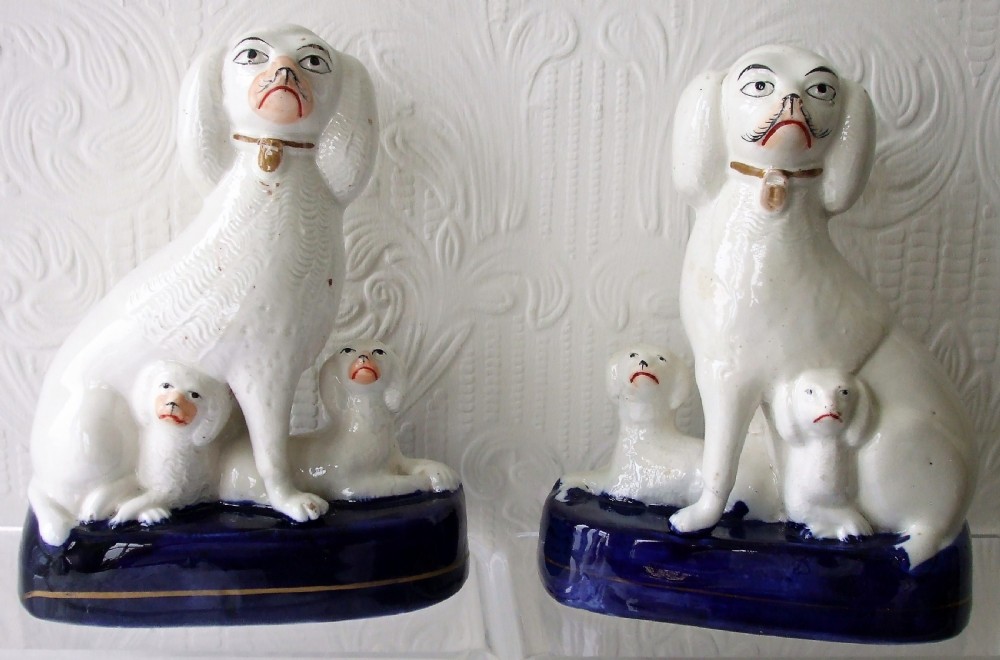 A pair of antique white glazed ceramic Staffordshire poodle dog figurines with small puppies resting on deep cobalt blue bases.