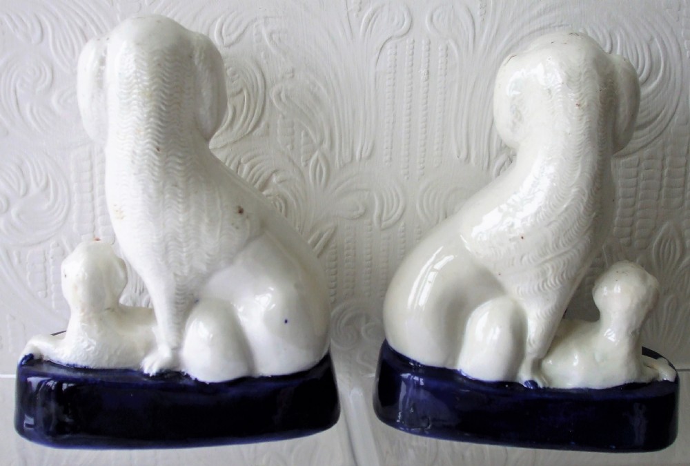 A pair of antique white glazed ceramic Staffordshire poodle dog figurines with small puppies resting on deep cobalt blue bases. View IV