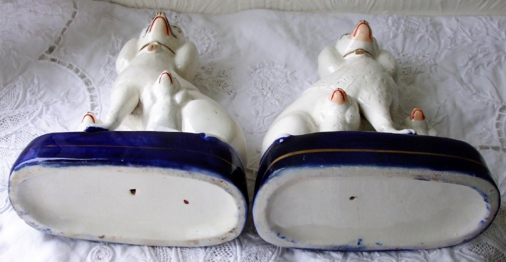 A pair of antique white glazed ceramic Staffordshire poodle dog figurines with small puppies resting on deep cobalt blue bases. View VII