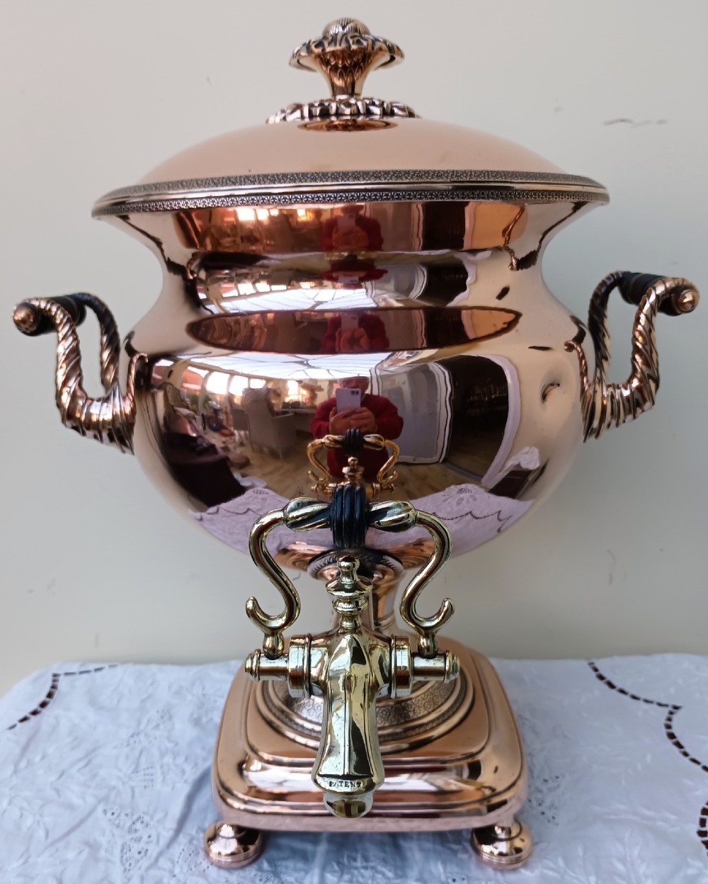 A polished Georgian copper tea urn featuring twin reeded handles, a brass spigot tap, and a square pedestal base resting on ball feet.