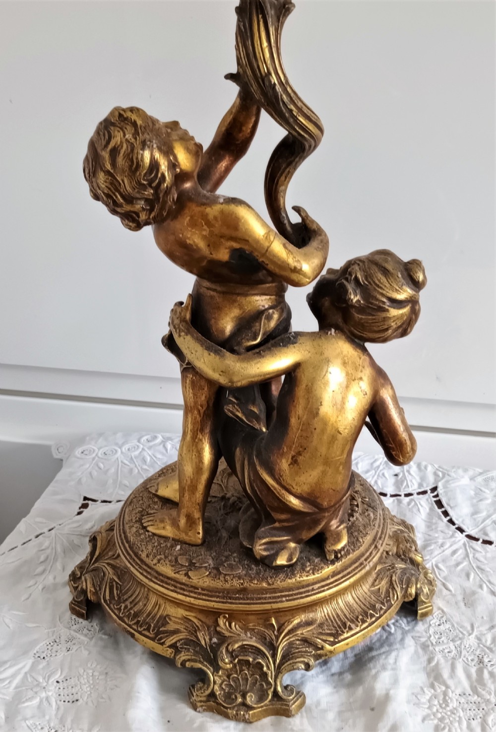 An antique Victorian oil lamp featuring a gilded metal base with sculpted cherubs, a green glass reservoir, and a yellow ruffled glass shade with chimney. View V