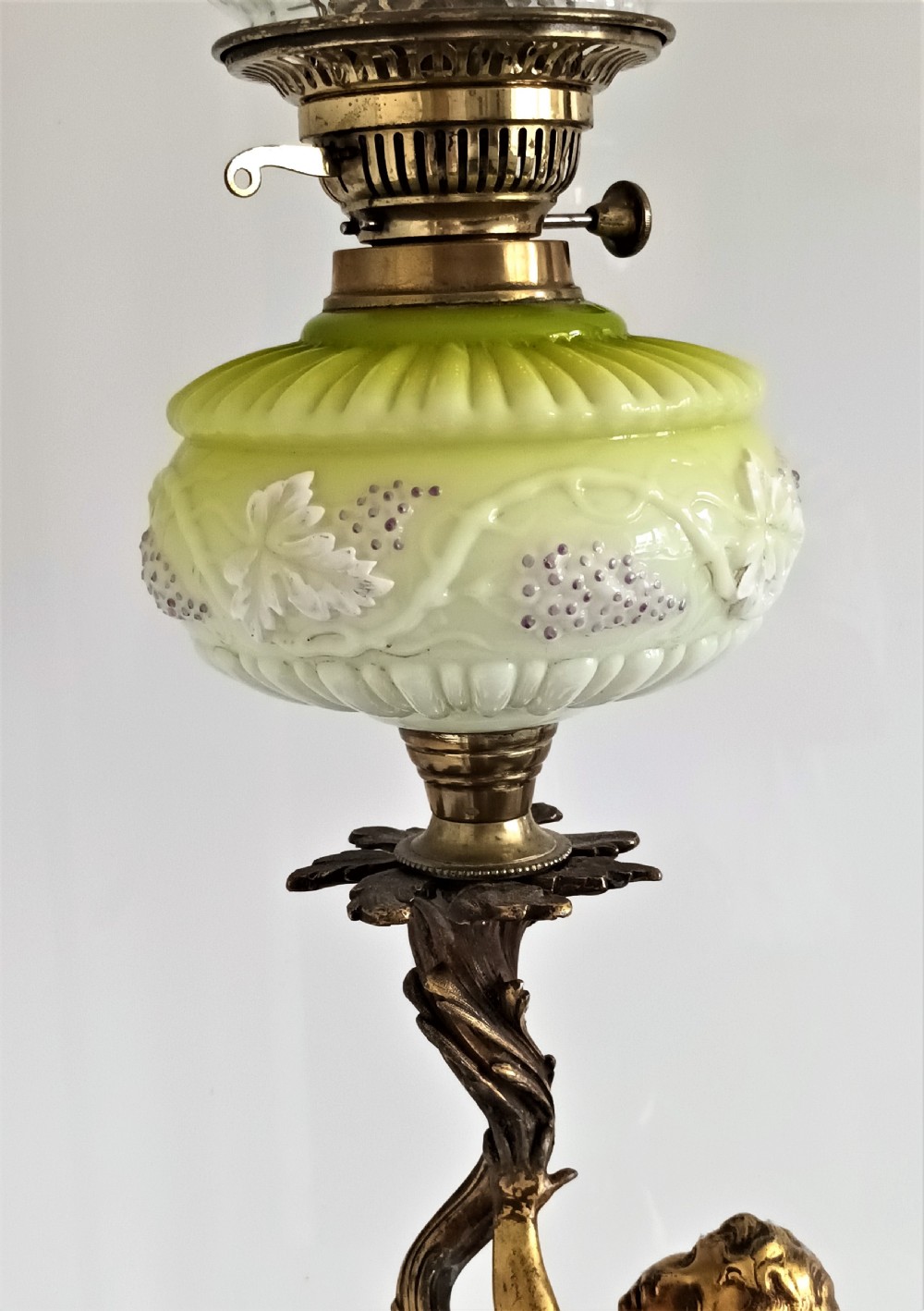 An antique Victorian oil lamp featuring a gilded metal base with sculpted cherubs, a green glass reservoir, and a yellow ruffled glass shade with chimney. View VI