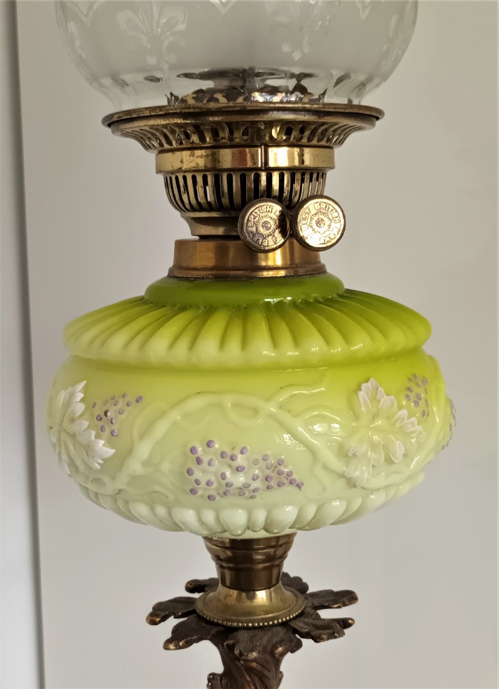 An antique Victorian oil lamp featuring a gilded metal base with sculpted cherubs, a green glass reservoir, and a yellow ruffled glass shade with chimney. View VII