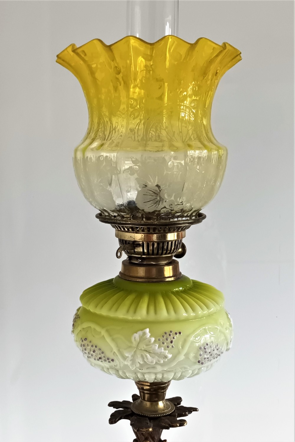 An antique Victorian oil lamp featuring a gilded metal base with sculpted cherubs, a green glass reservoir, and a yellow ruffled glass shade with chimney. View VIII