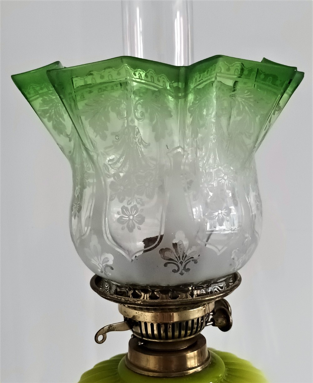 An antique Victorian oil lamp featuring a gilded metal base with sculpted cherubs, a green glass reservoir, and a yellow ruffled glass shade with chimney. View XII