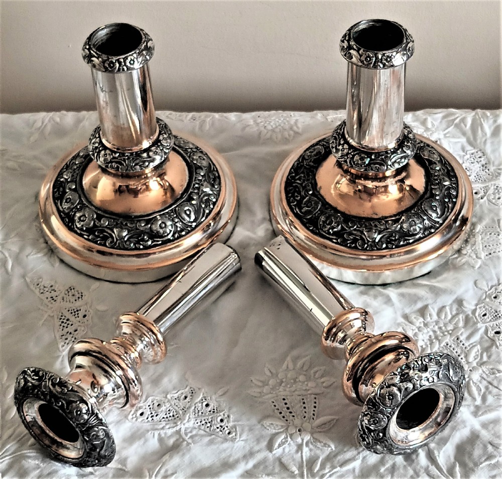 A pair of Georgian Old Sheffield Plate telescopic candlesticks featuring extendable silver columns showing copper undertones and ornate embossed borders. View II