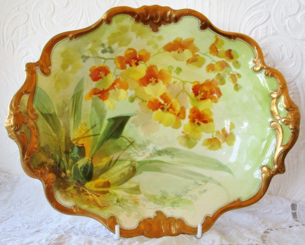 An oval antique Royal Doulton porcelain dish featuring hand-painted yellow orchids on a pale green ground with a gilded scroll border.