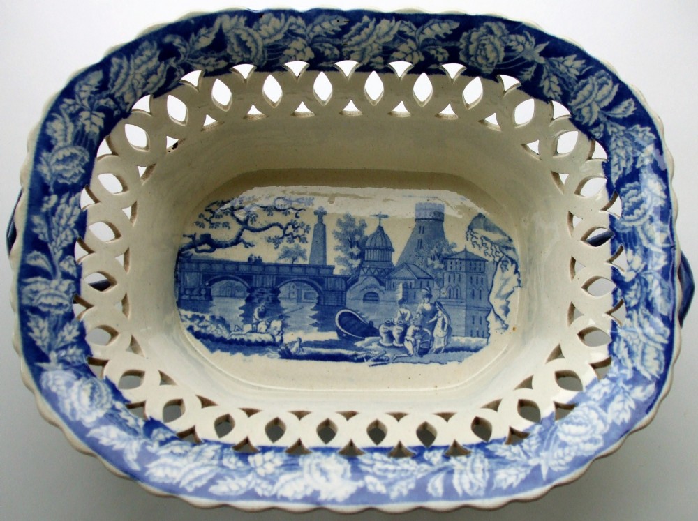 An oval Georgian blue and white ceramic chestnut basket featuring pierced lattice sides, a floral rim, and a central transfer-printed river landscape.