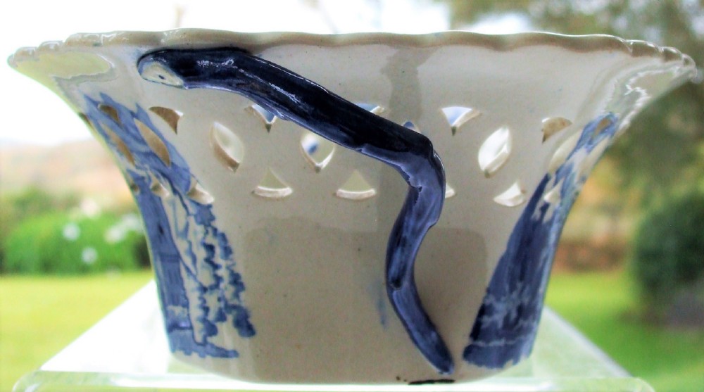 An oval Georgian blue and white ceramic chestnut basket featuring pierced lattice sides, a floral rim, and a central transfer-printed river landscape. View V
