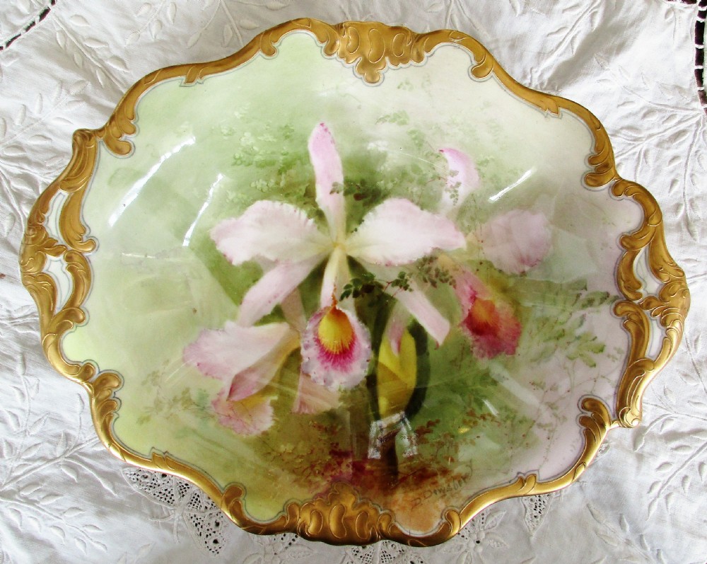 An oval antique porcelain dish featuring hand-painted pink orchids on a pale green ground with a gilded scrolled rim.