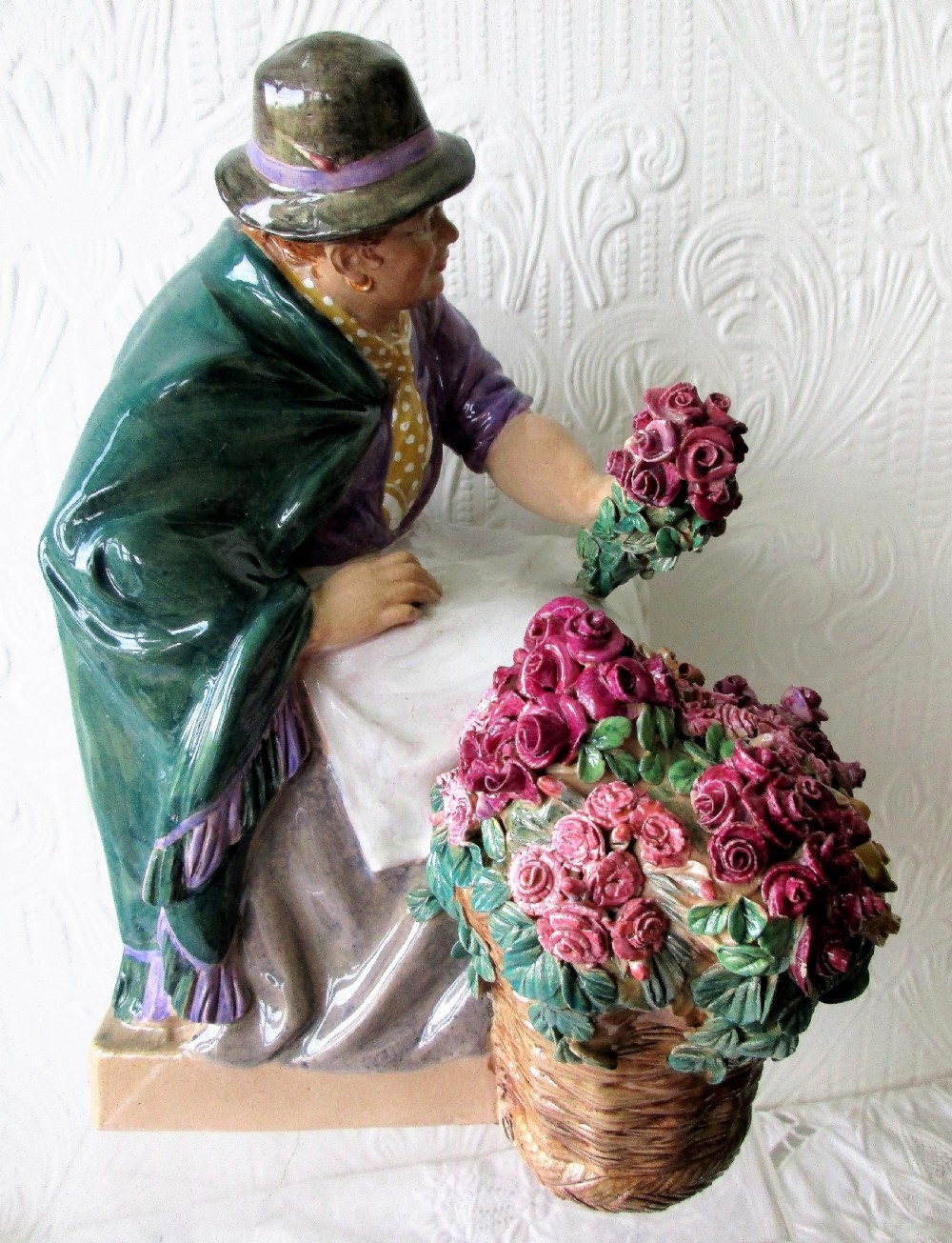 A polychrome glazed earthenware figurine depicting a seated woman wearing a green shawl and purple top holding a bouquet of red roses next to a basket full of flowers. View V
