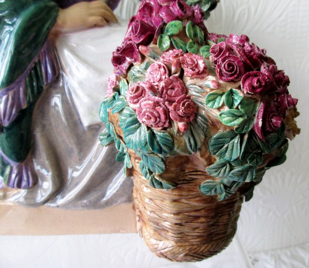 A polychrome glazed earthenware figurine depicting a seated woman wearing a green shawl and purple top holding a bouquet of red roses next to a basket full of flowers. View VI