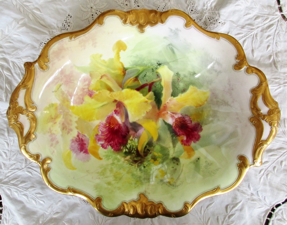 An oval antique porcelain cabinet dish featuring hand-painted yellow and pink orchids with elaborate gilded scrollwork borders.