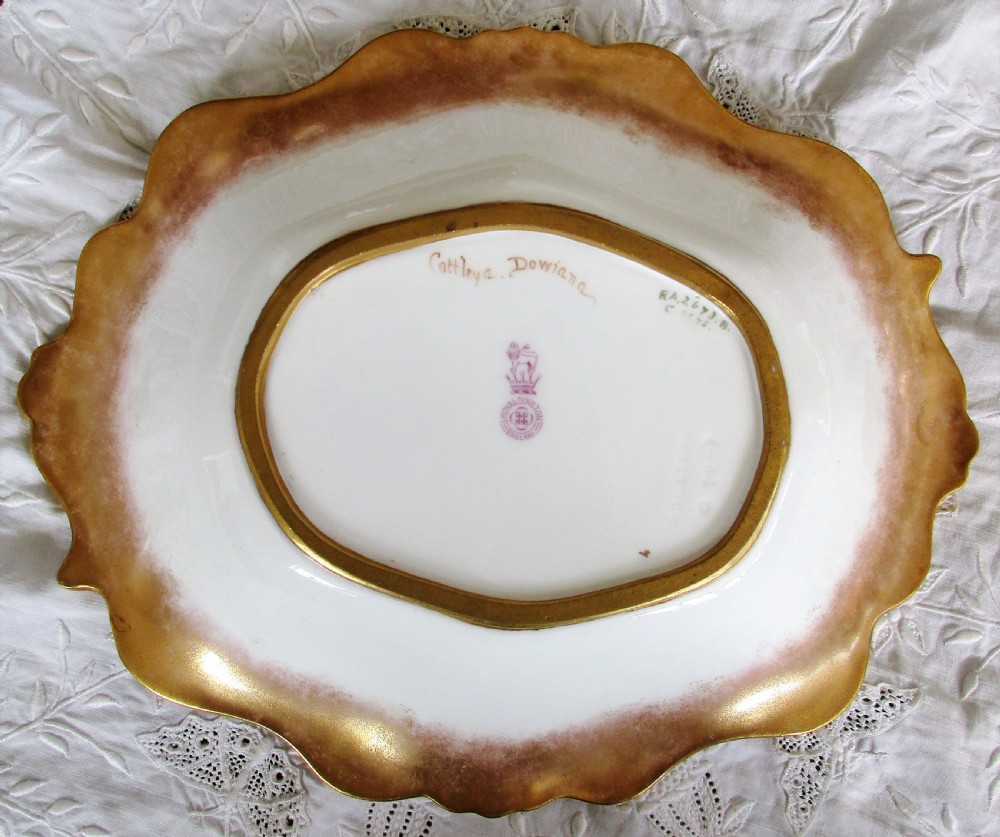 An oval antique porcelain cabinet dish featuring hand-painted yellow and pink orchids with elaborate gilded scrollwork borders. View III