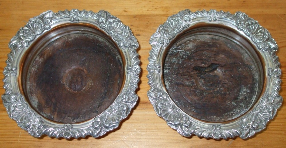 A pair of antique Georgian Old Sheffield Plate wine coasters featuring ornate relief borders and turned wood centres with exposed copper tone. View II