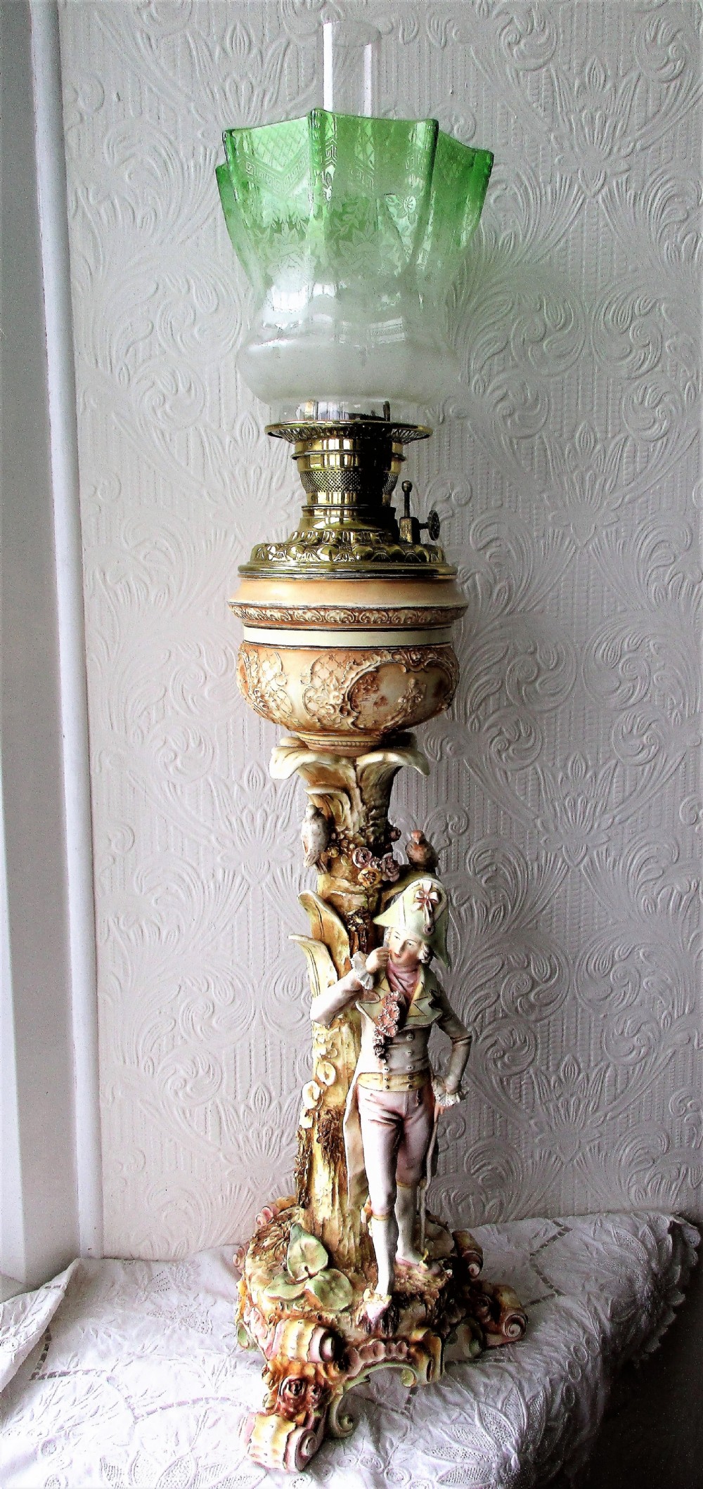 An antique Victorian porcelain oil lamp featuring a sculpted male figurine base, relief reservoir, brass burner, and a fluted green glass shade.