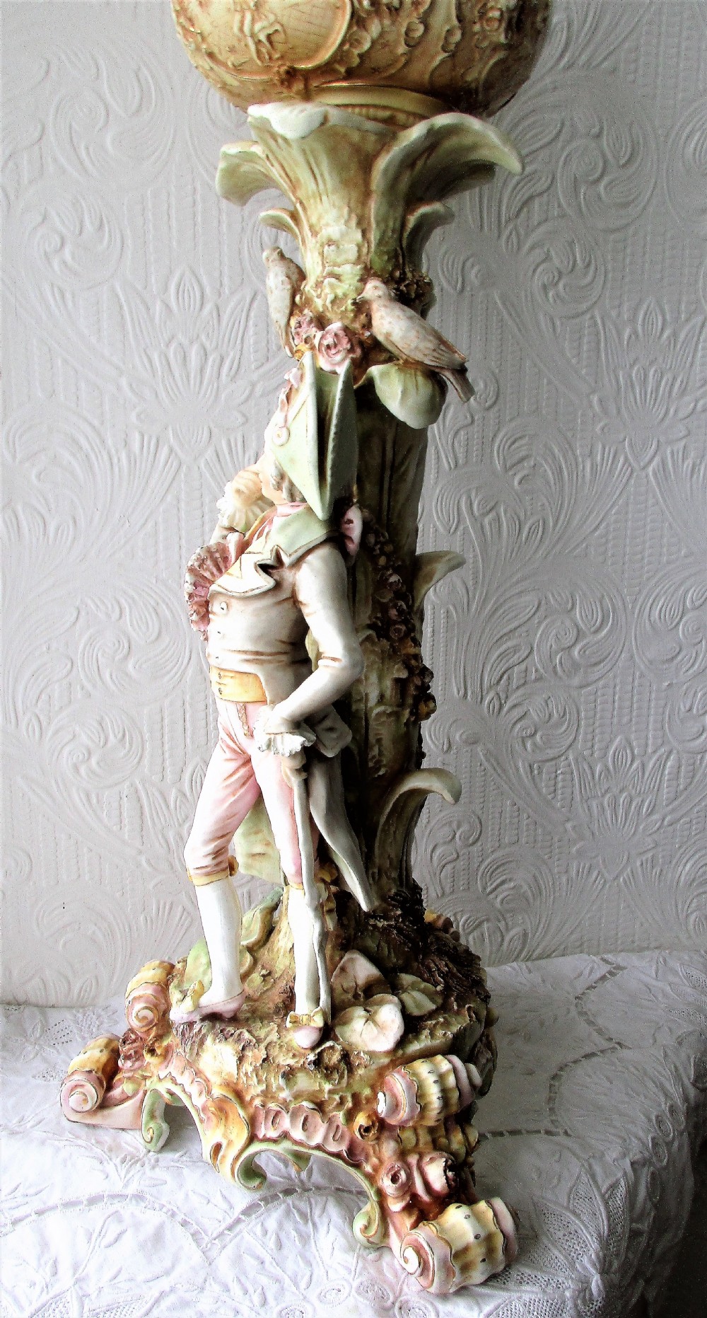 An antique Victorian porcelain oil lamp featuring a sculpted male figurine base, relief reservoir, brass burner, and a fluted green glass shade. View III