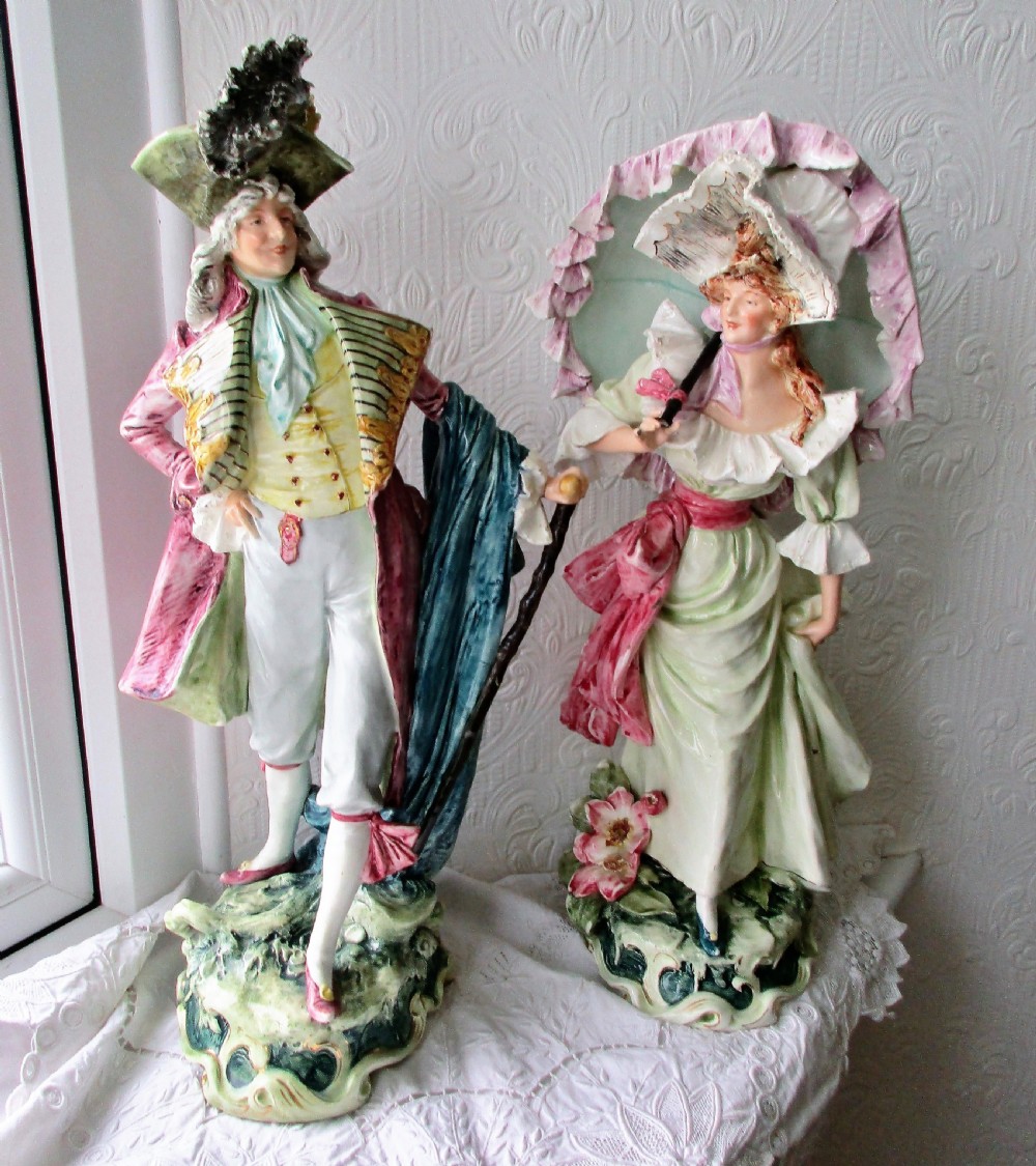 A pair of hand-painted French faience ceramic figurines depicting an 18th-century gentleman and a lady holding a parasol.