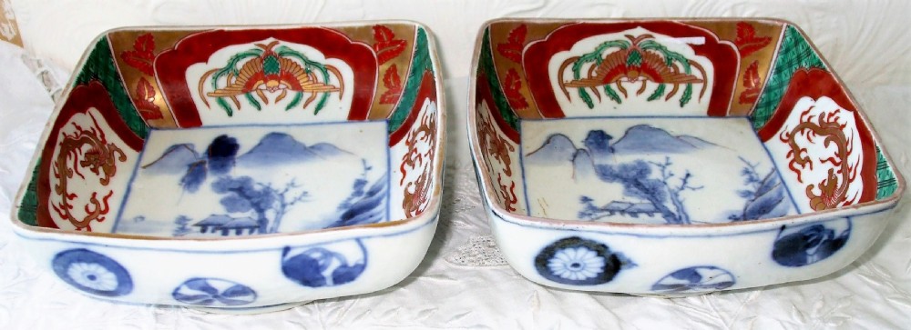 A pair of square Japanese Imari porcelain dishes featuring underglaze blue landscape scenes encircled by iron-red, green, and gold enamel borders. View II