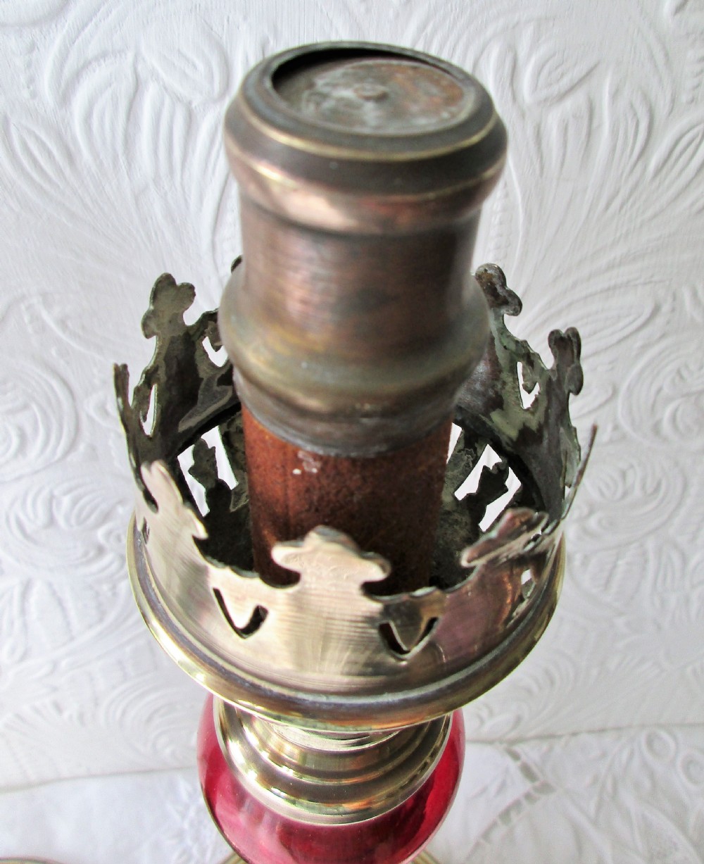 A pair of Victorian brass candle lamps featuring hand-painted floral enamel on red cranberry glass shades and stems. View V