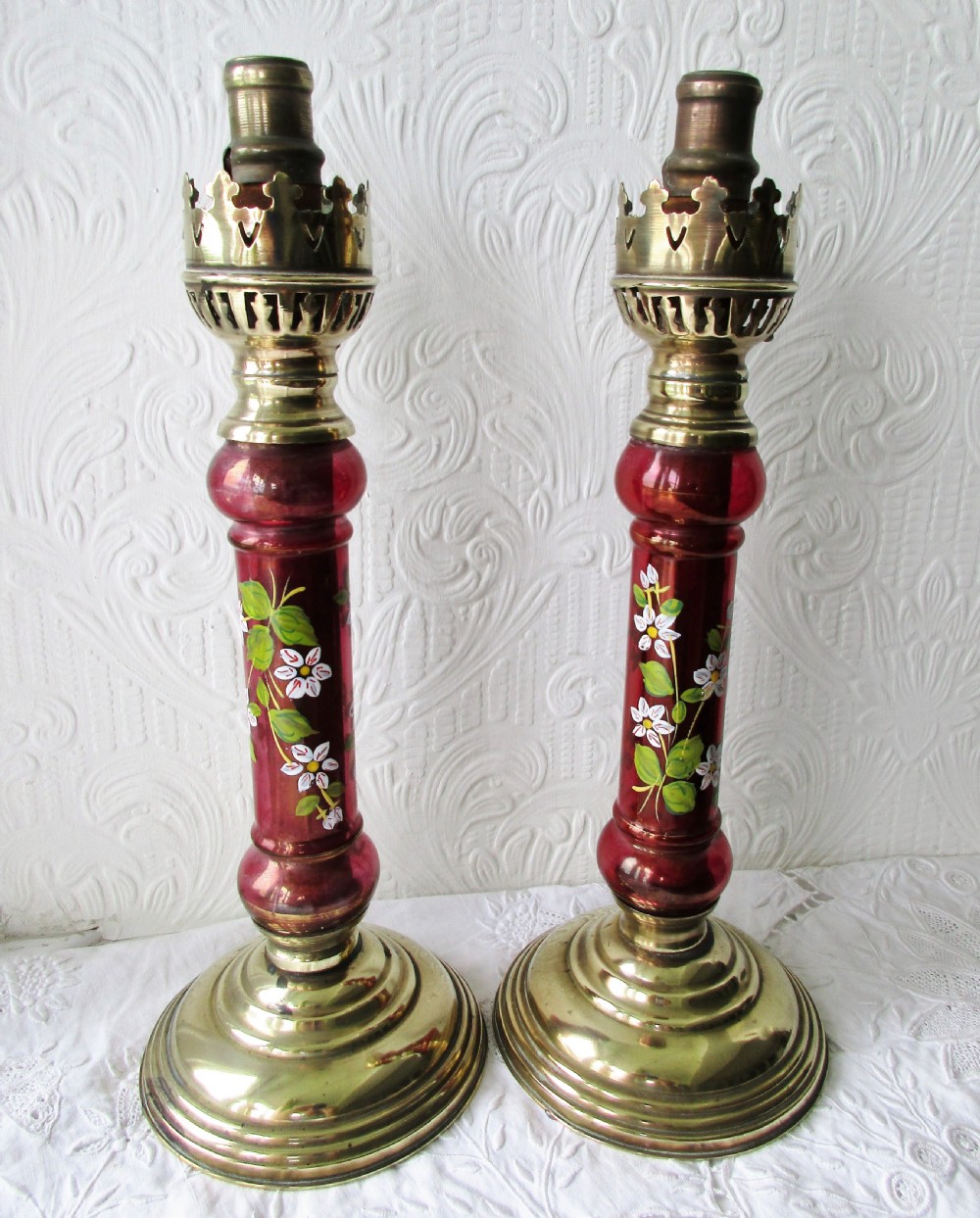 A pair of Victorian brass candle lamps featuring hand-painted floral enamel on red cranberry glass shades and stems. View VI