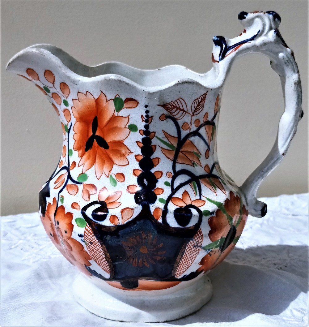 An antique Victorian Gaudy Welsh earthenware jug decorated with hand-painted orange floral motifs, cobalt blue details, a scalloped rim, and a molded handle.