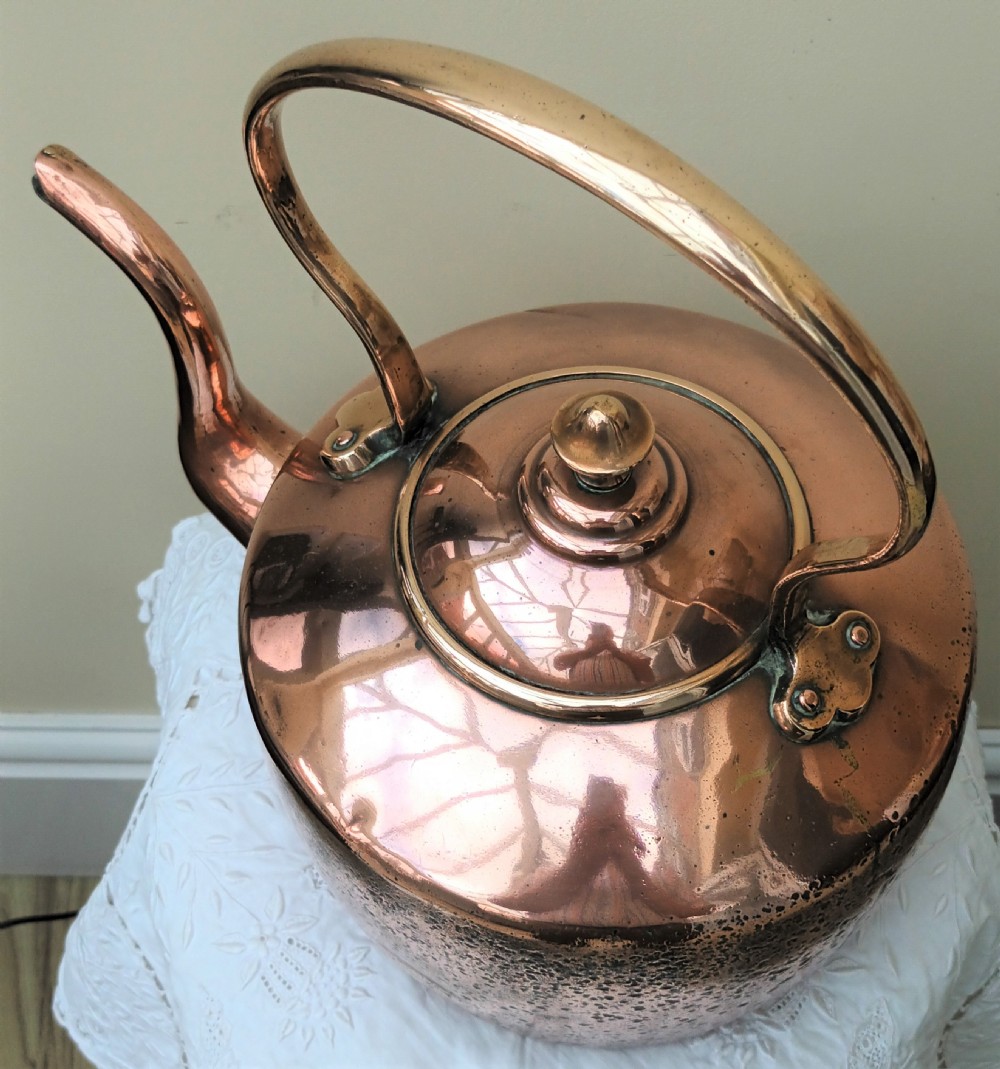 An antique Victorian copper kettle featuring a gooseneck spout, a fixed overhead loop handle, and a domed lid topped with a brass finial. View V