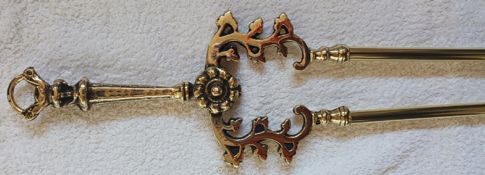 A set of three polished brass Victorian fire irons comprising a shovel with pierced detailing, a poker, and a pair of tongs with decorative scrollwork handles. View IX