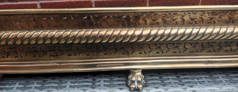 A Victorian pierced brass fireplace fender with central rope-twist moulding, pierced fretwork bands, and cast paw feet. View V