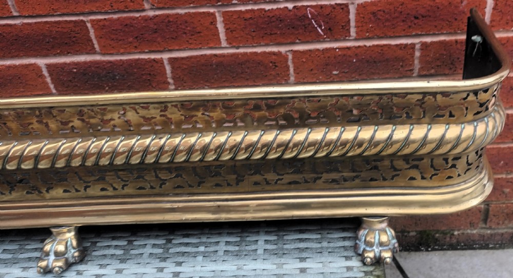 A Victorian pierced brass fireplace fender with central rope-twist moulding, pierced fretwork bands, and cast paw feet. View VI