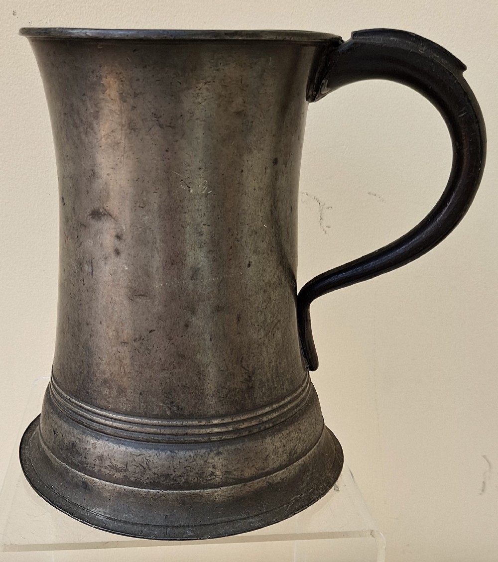 An antique Victorian pewter quart mug featuring a concave body, a flared moulded base, and a dark curved handle.