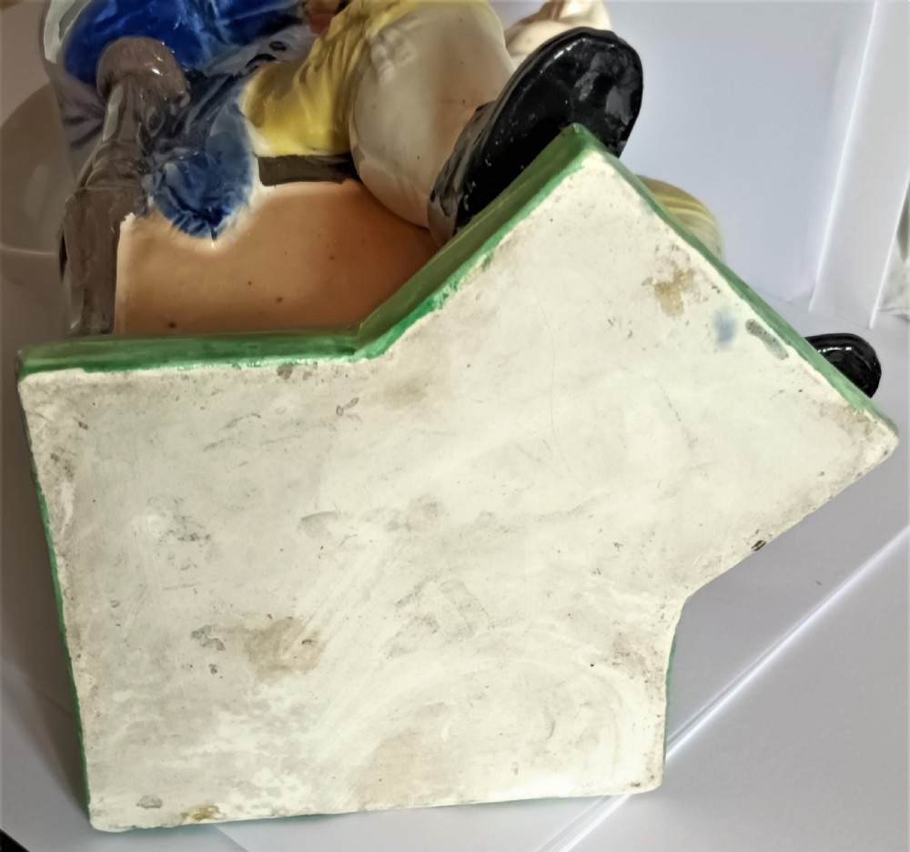 An antique Staffordshire earthenware Toby Jug depicting a seated squire wearing a black tricorn hat, blue coat, red waistcoat, and yellow breeches. View V